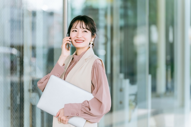 ビルの前で携帯で仕事の話しているピンクの服を着た女性