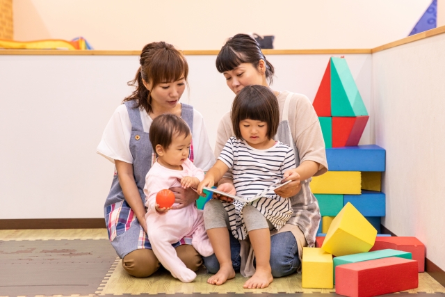 子供に本を読む保育士女性2人